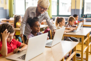 kinderen met laptop in de klas met een leerkracht erbij