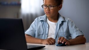 jongen kijkt met bedrukt gezicht naar beeldscherm laptop