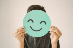 teen boy holding smile emoji face cover his face
